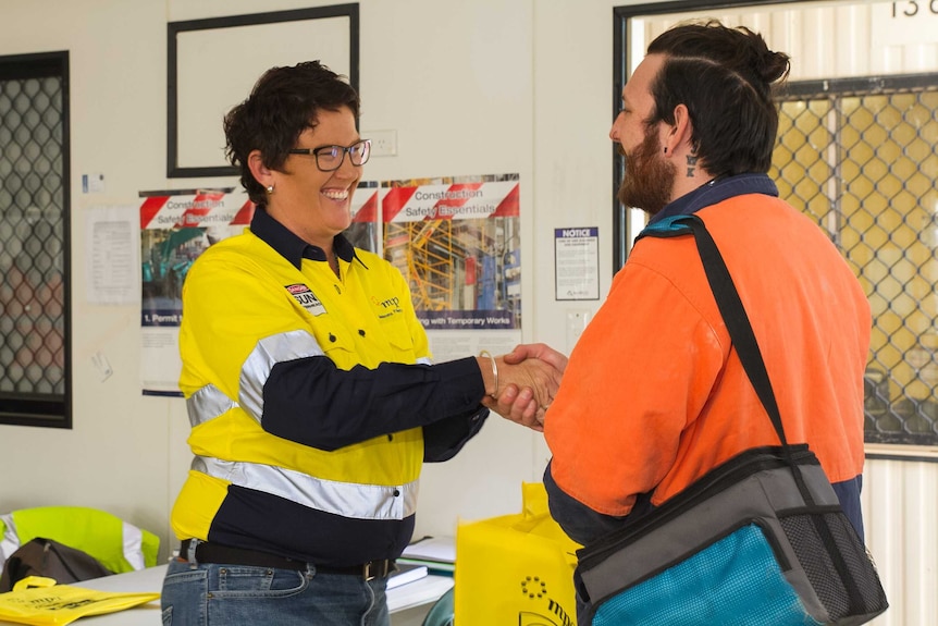 Jo Crotty, wearing a yellow high-vis short, shakes the hand of a construction worker.