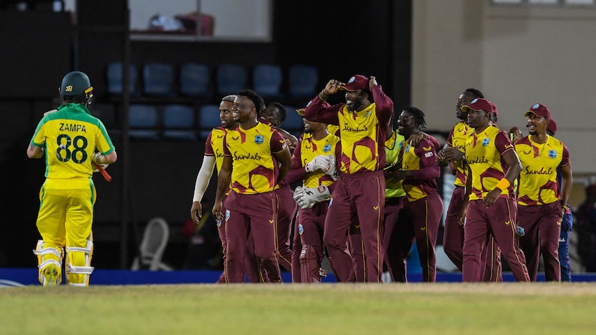 An Australian batsman trudges off as the West Indies cricketers celebrate victory on the oval.