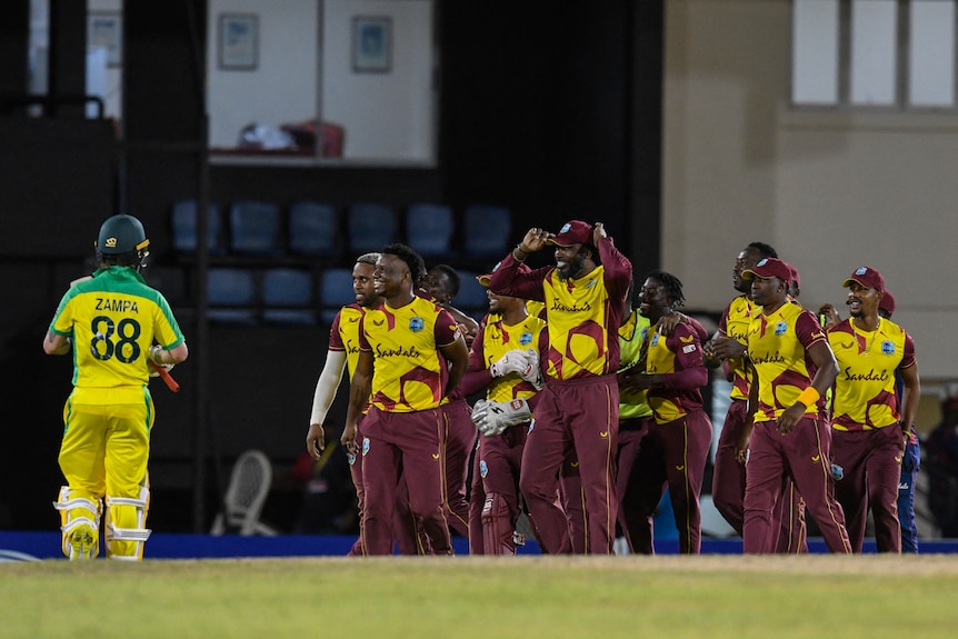 An Australian batsman trudges off as the West Indies cricketers celebrate victory on the oval.