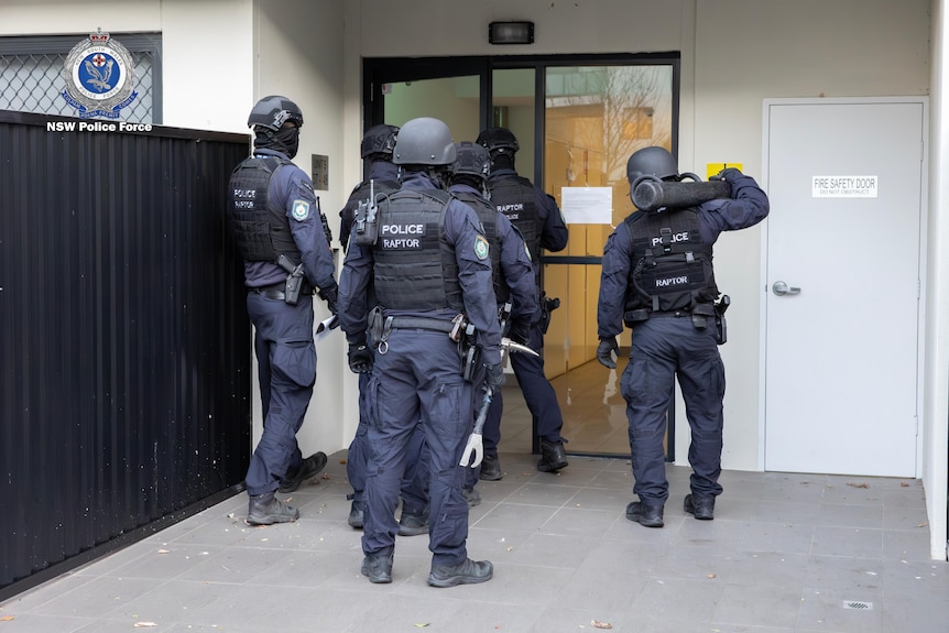 nsw police officers part of taskforce magnus outside a unit about to enter to conduct an arrest