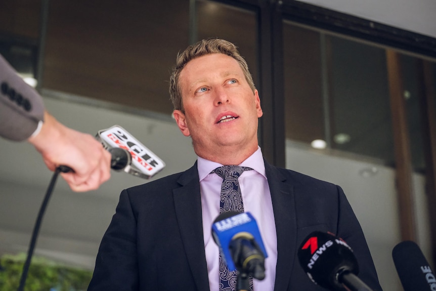 a man talking outdoors to the media