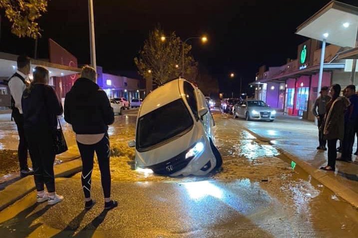 A car protruding out of the ground as bystanders watch.