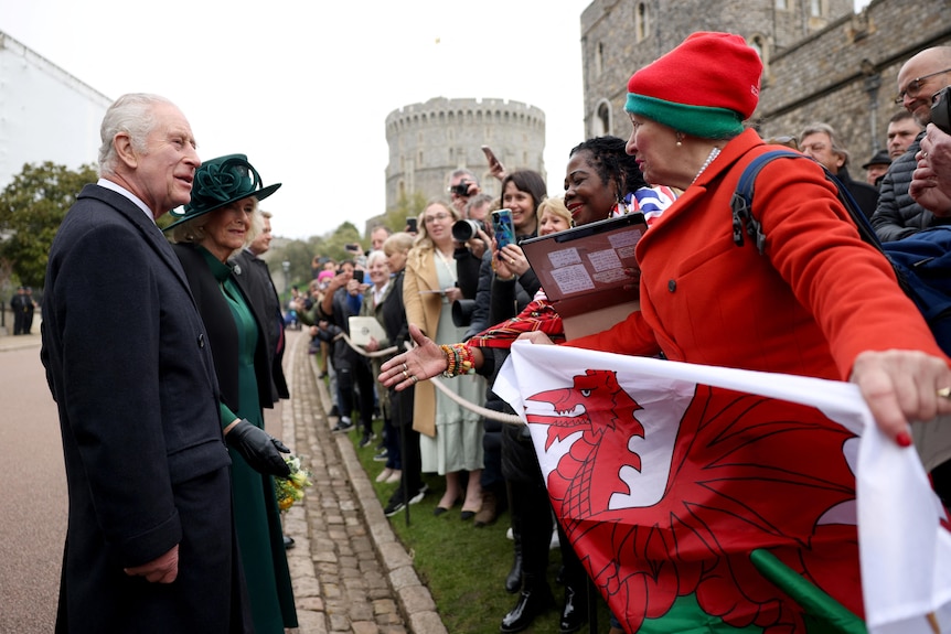 A woman holding a Welsh flag speaks to King Charles and Queen Camilla.