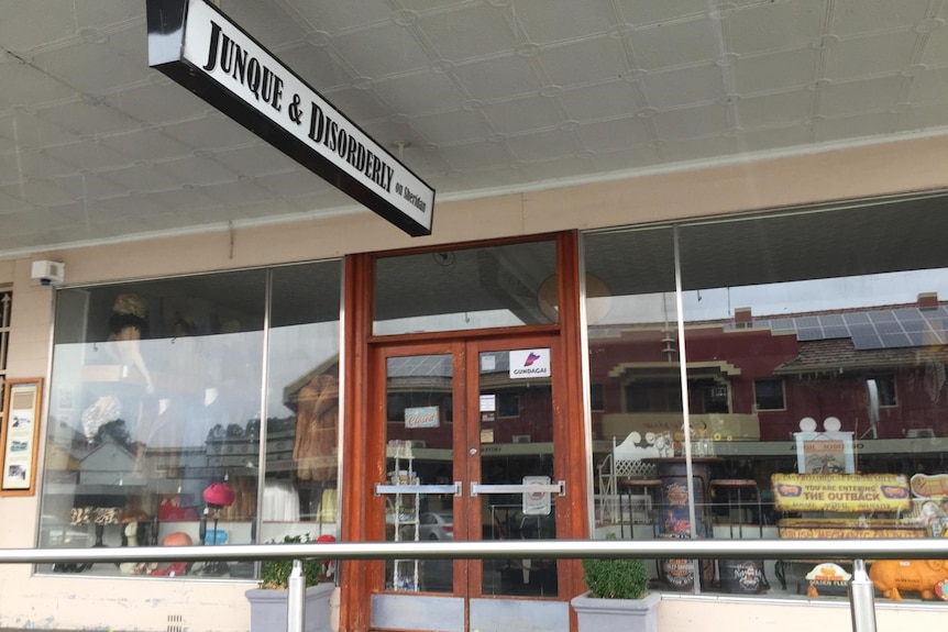 Shop front with full glass windows and wooden door frome. Sign "Junque and Disorderly on Sheahan"