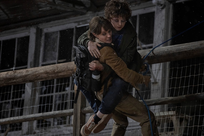 Film still of Angelina Jolie as Hannah holding Finn Little as Connor climbing down a wall from Those Who Wish Me Dead