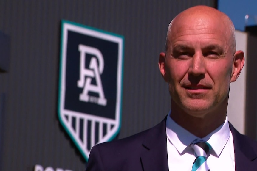 Man smiling in front of Port Adelaide Football Club logo.