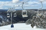 A chairlift over hills scattered with snow. Icicles hang off the chairs on the chairlift.