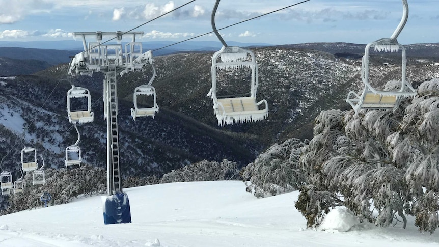 A chairlift over hills scattered with snow. Icicles hang off the chairs on the chairlift.