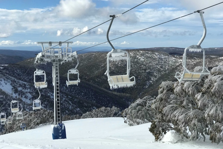 A chairlift over hills scattered with snow. Icicles hang off the chairs on the chairlift.