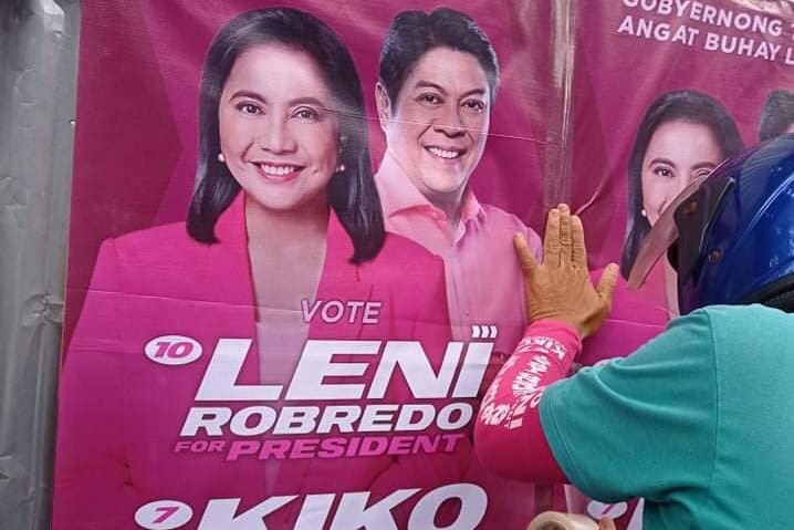A pink poster with Ms Robredo and her running mate being stuck onto a wall.