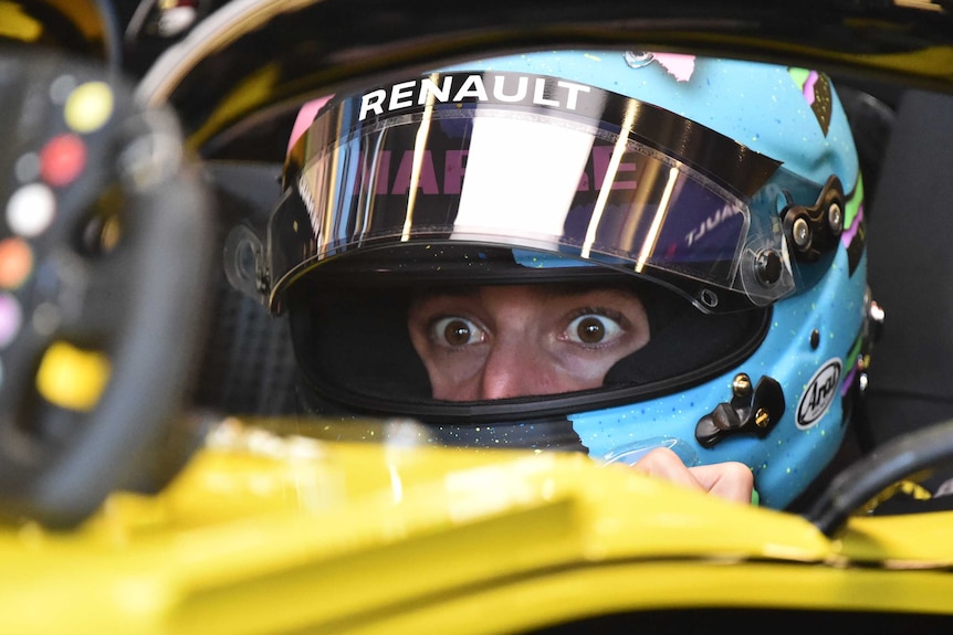 Daniel Ricciardo's wide and surprised eyes are visible through the visor of his helmet as he sits in his car.