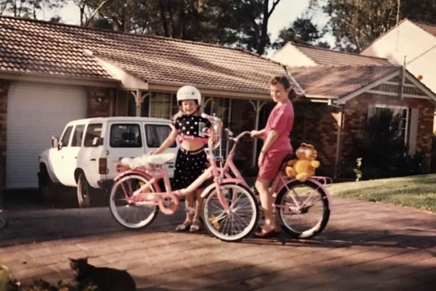 A young Rebel Wilson and another girl with bikes outside a family home.