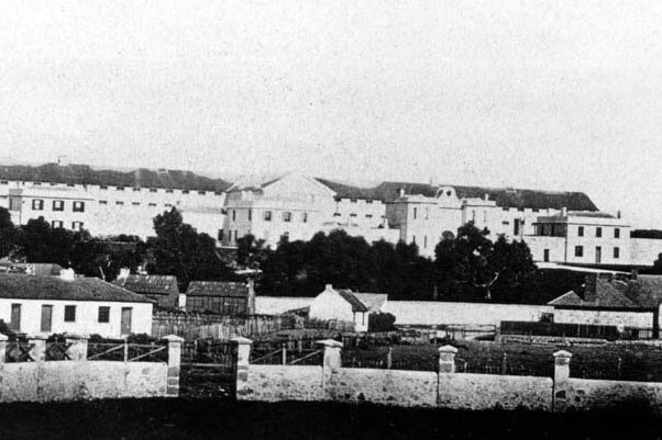 Old black and white photo of Fremantle prison and surrounding houses with limestone wall