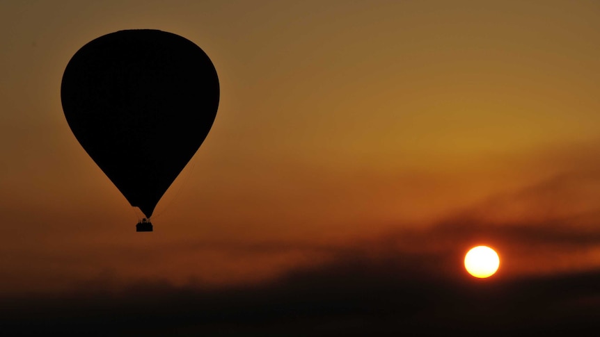 A hot air balloon flies over the West Bank in Luxor, Egypt, in front of the setting sun.