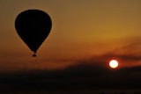 A hot air balloon flies over the West Bank in Luxor, Egypt, in front of the setting sun.