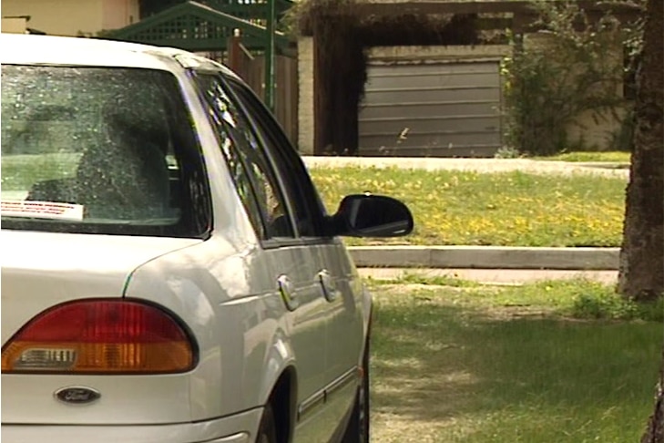 Rear shot of a white sedan parked across the road from a house.