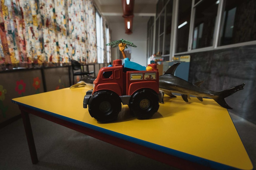 Children's toys including a truck and a shark sit on a yellow table at Princess Margaret Hospital.