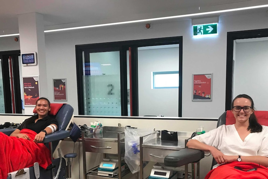 Two females sit next to each other in blood donation chairs looking at the camera