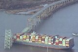 An aerial view of a steel truss bridge that has fallen on top of a container ship in a river.