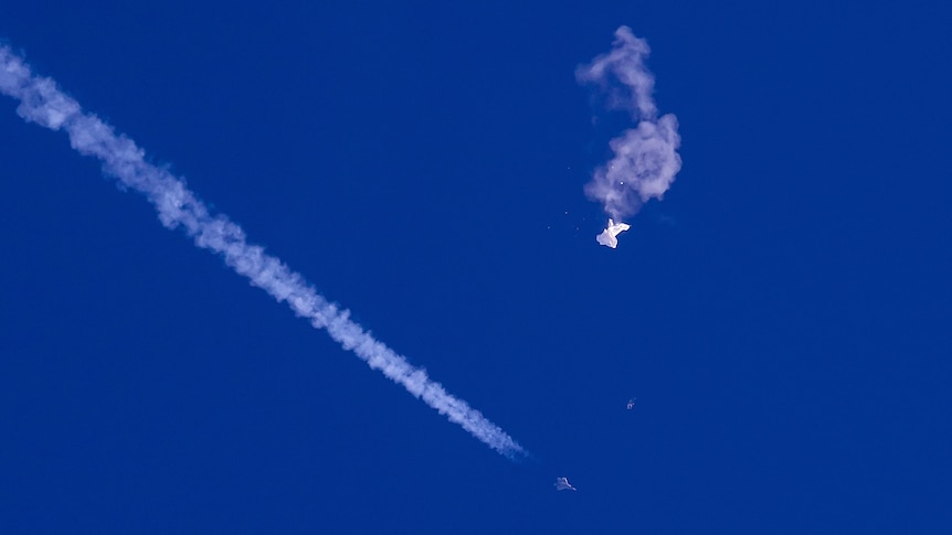 Remnant of Chinese balloon drifting in sky as fighter jet and its trail seen nearby.