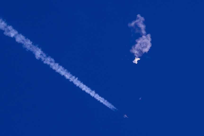 Remnant of Chinese balloon drifting in sky as fighter jet and its trail seen nearby.