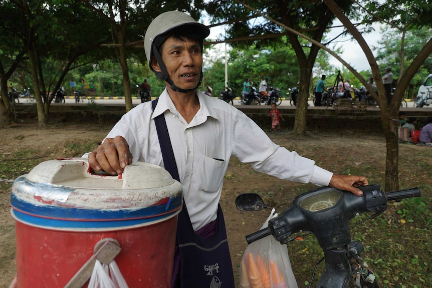 Tin Tun Aung stands with his bucket of ice cream, cones and his motorcycle near the market