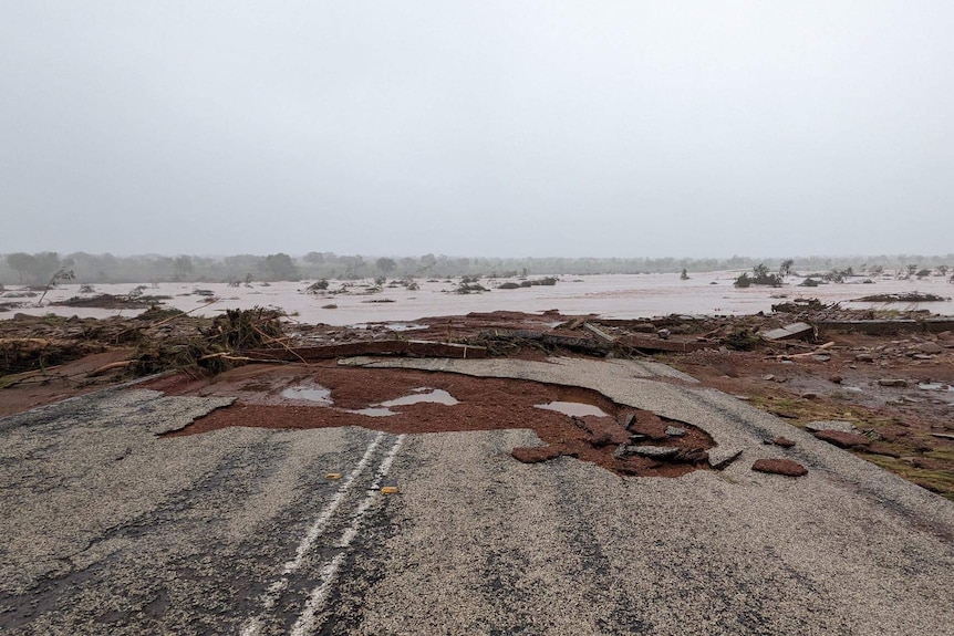 A large hole in a road, with flooding in the distance. 