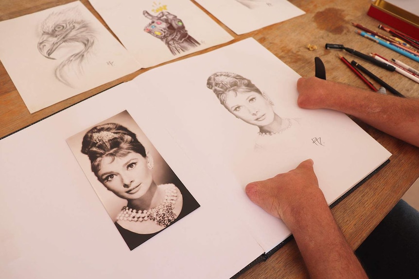 Three pencil sketches and a photo on a table of art supplies.