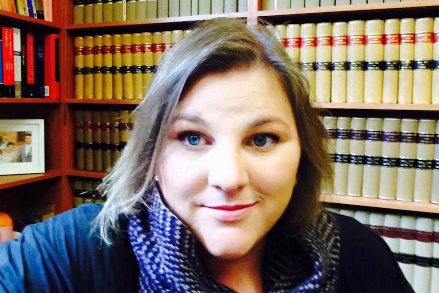 A woman smiles at the camera sitting front of a shelf full of books.