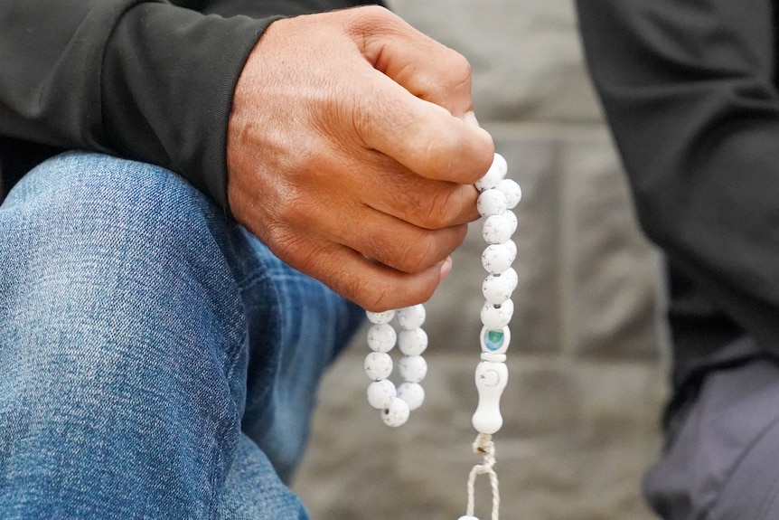 A man's hands holding a small string of beads, seen from close up