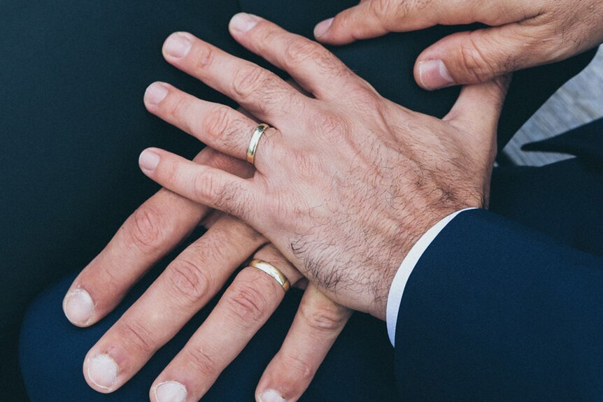 Two men's hands touching, each hand showing a wedding ring