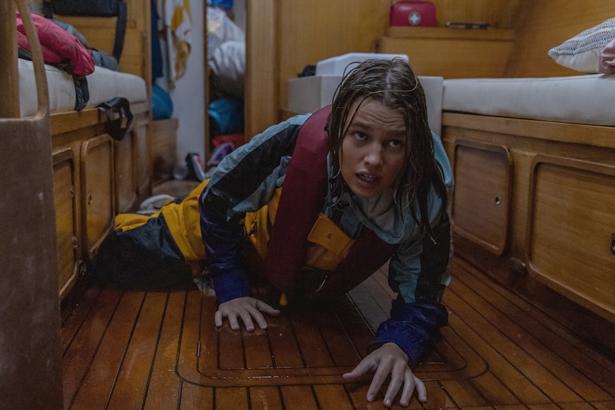 Teagan Croft, as Jessica Watson, crawls on the floor of her boat as water gushes in during a storm.