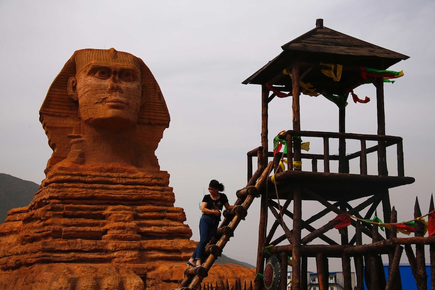 A woman climbs a tower in front of a full-scale replica of the Sphinx, which is part of an unfinished theme park in China.