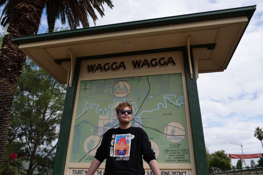 A man sits on a pole in front of a large sign with a map of Wagga Wagga.