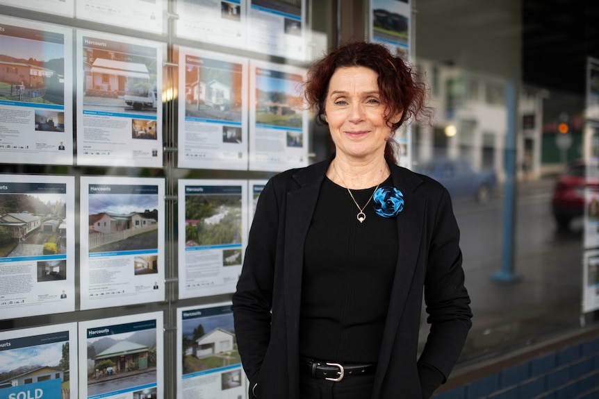 A woman with dark hair stands in front of a real estate window