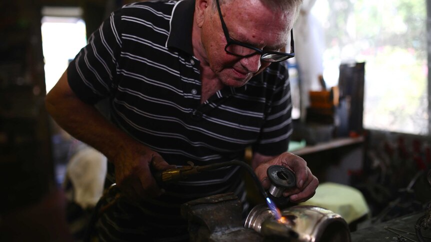 A man welding an antique metal fruit bowl stand in a workshop.