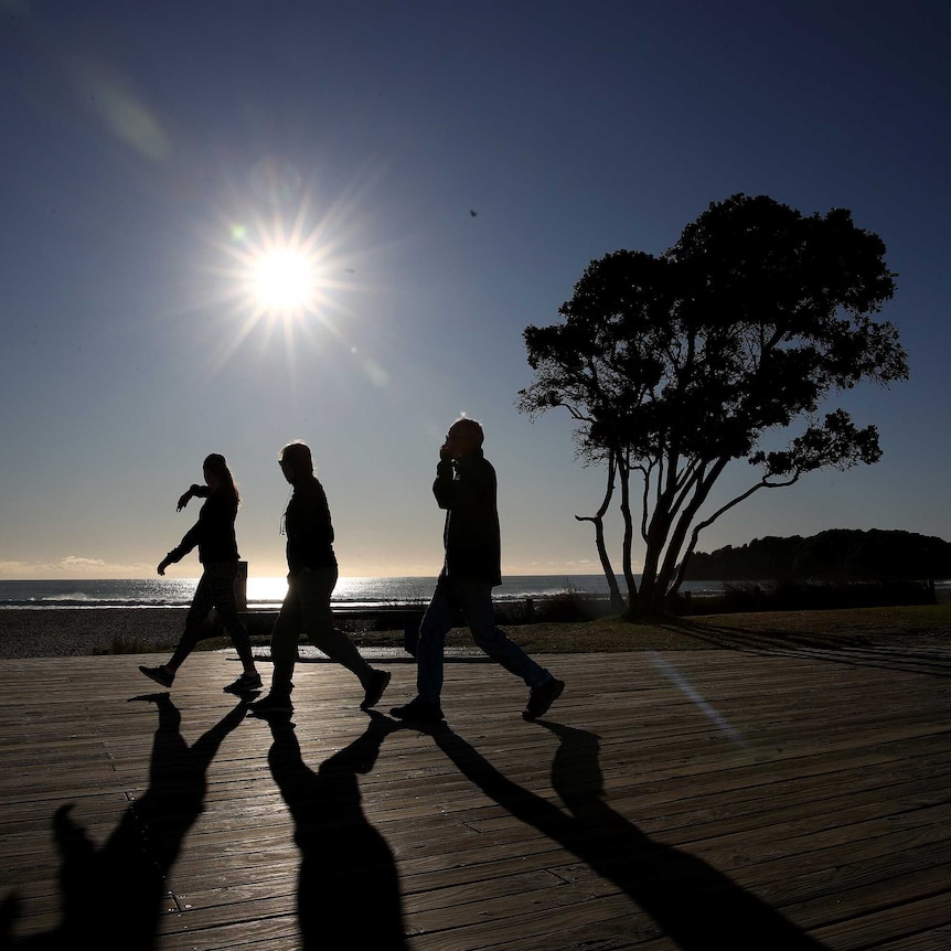 Three people in silhouette against a low sun walking along a beach esplanade