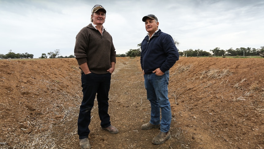 Two farmers stand in an empty irrigation channel.