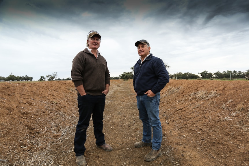 Two farmers stand in an empty irrigation channel.