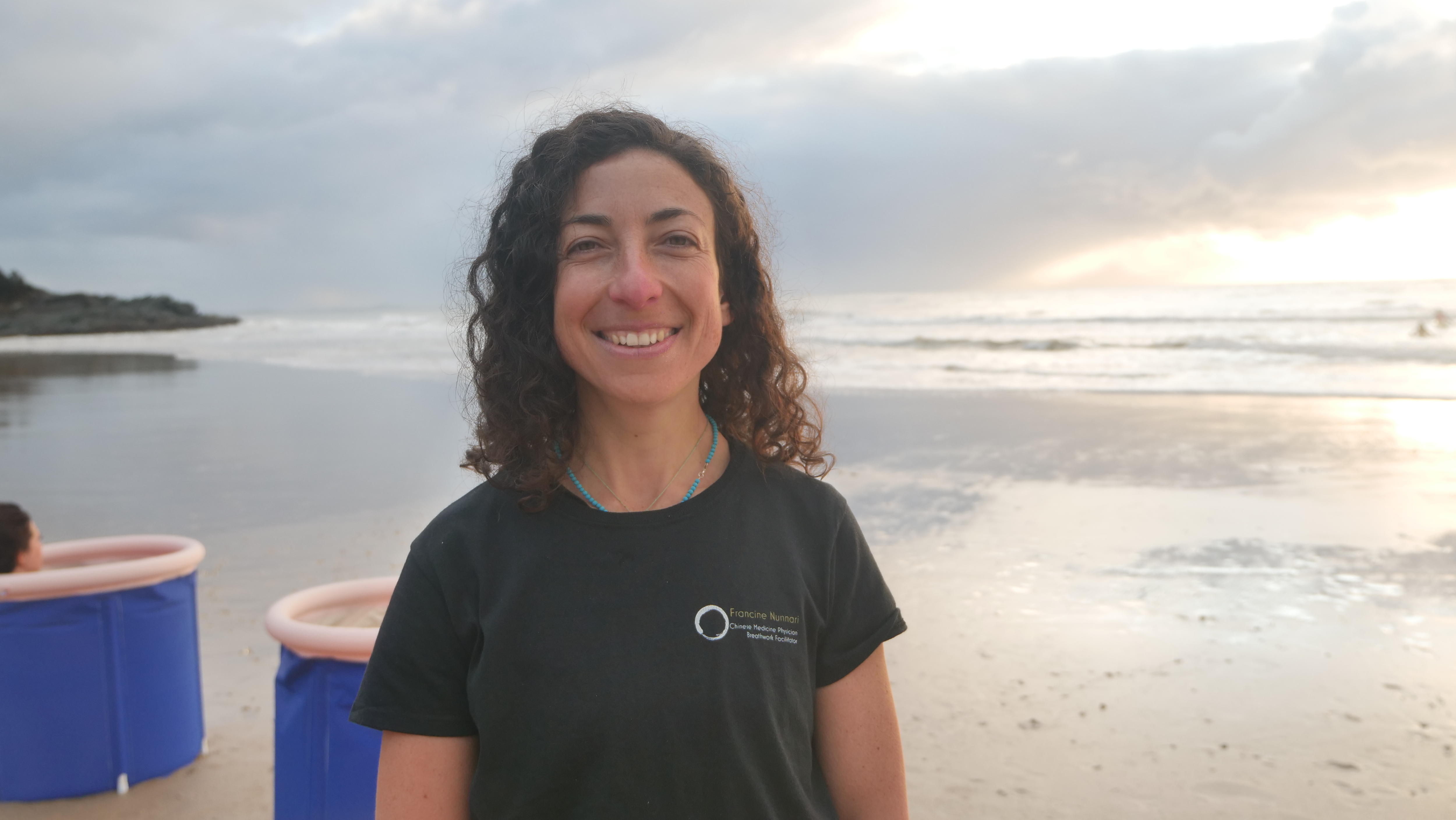 A woman in a black t-shirt smiles happily on a beach in front of some portable baths