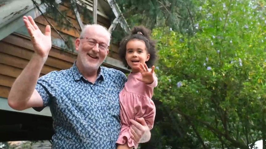 Grandfather holding his granddaughter, both smiling to camera