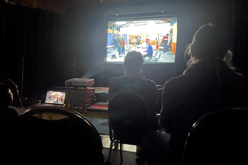 Dark room, people watch movie play on projector