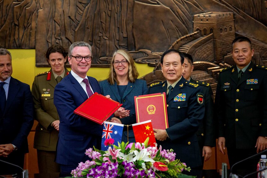 The two ministers face the cameras as they shake hands in front of Australian and Chinese defence officials.