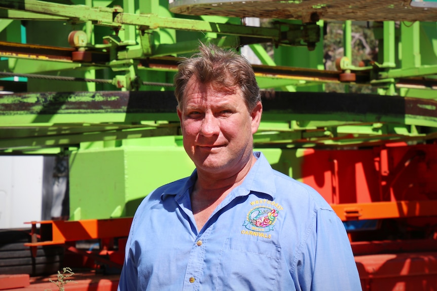 A man in a blue shirt stands in front of amusement ride equipment