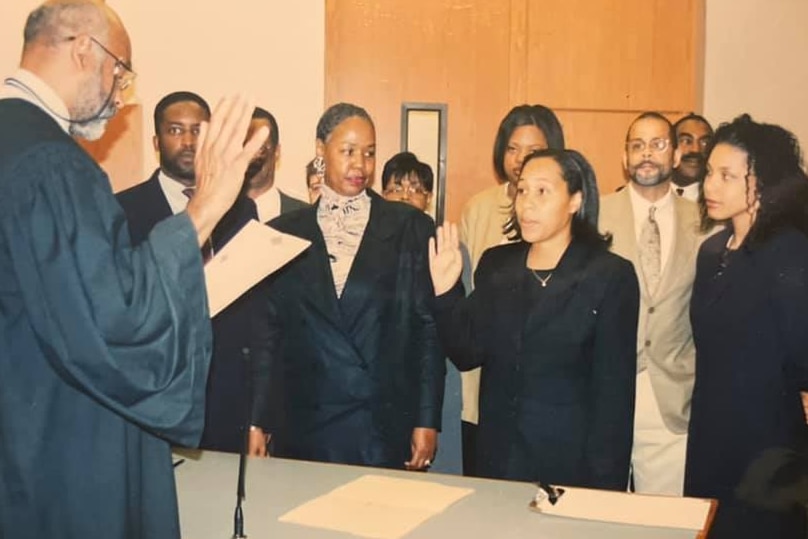 An old photo of a black woman in a black suit being sworn in as an assistant solicitor in Atlanta surrounded by black colleagues