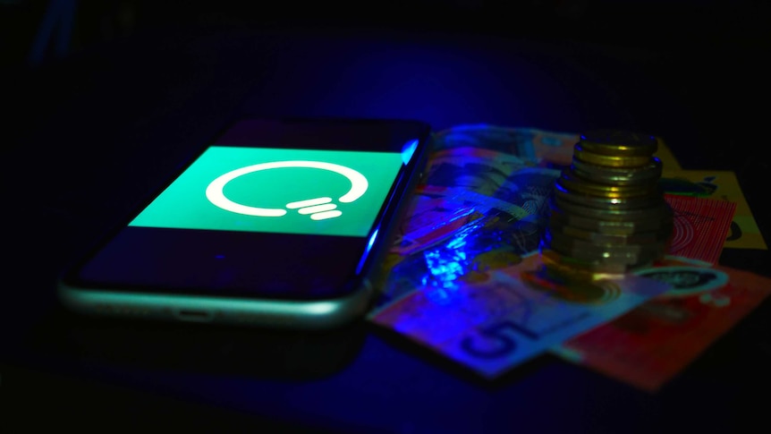 A pile of change and banknotes next to a mobile phone displaying a cryptocurrency logo.