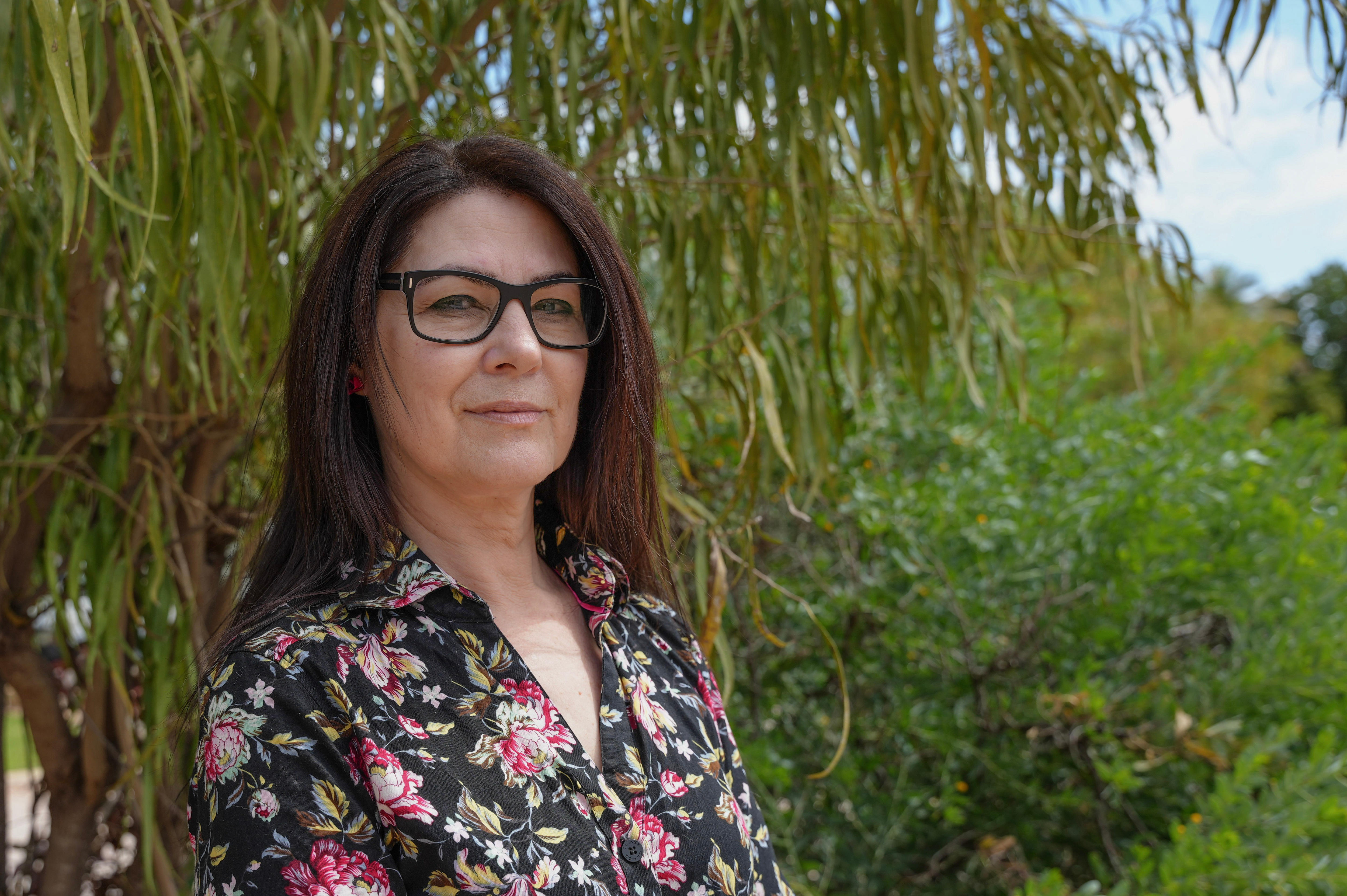 a woman with dark hair and glasses wearing a floral shirt smiling 