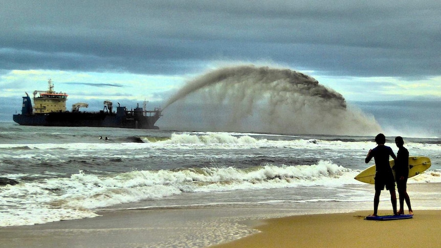 A large boat dredges sand from the ocean and fires it onto the shore.