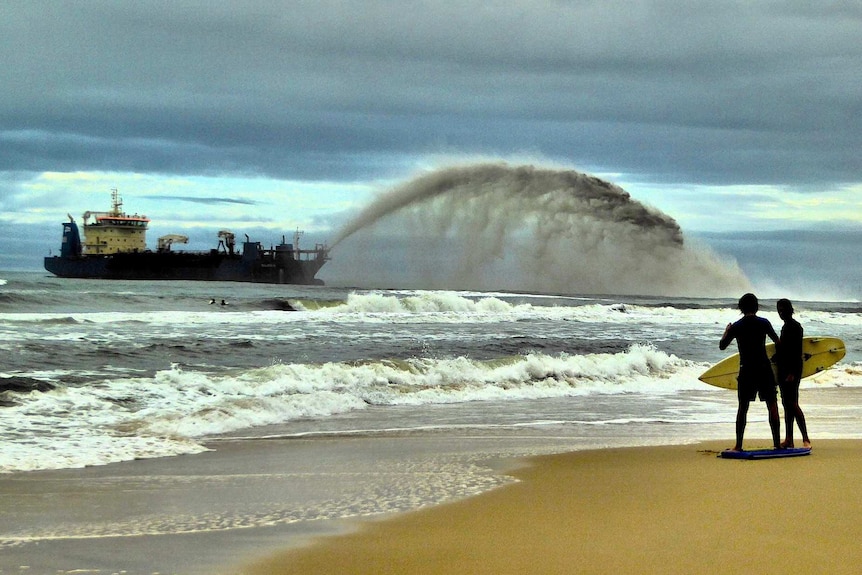 Un grand bateau drague le sable de l'océan et le projette sur le rivage.