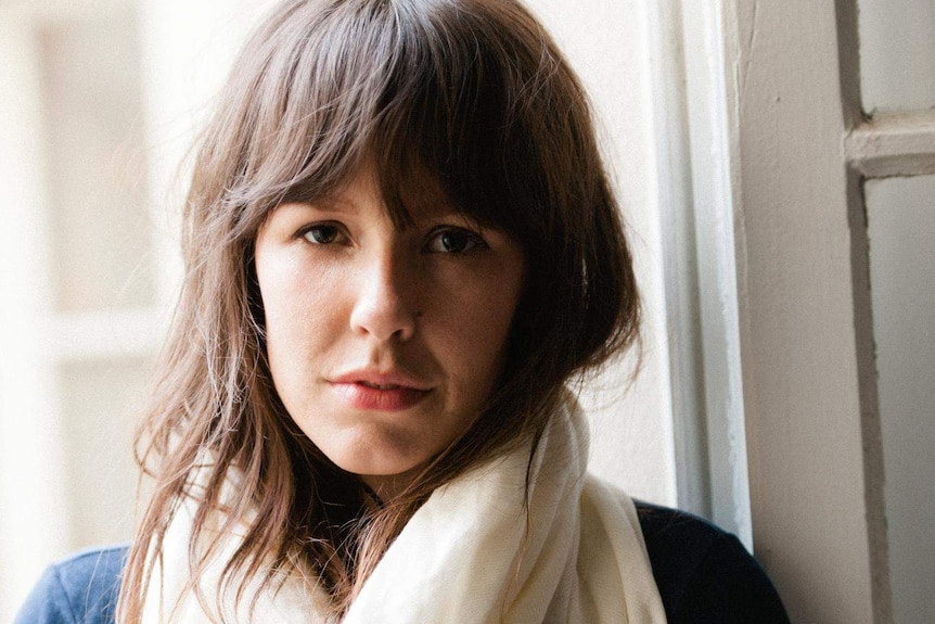 The author, a young woman with long brown hair and brown eyes, standing in front of a window.